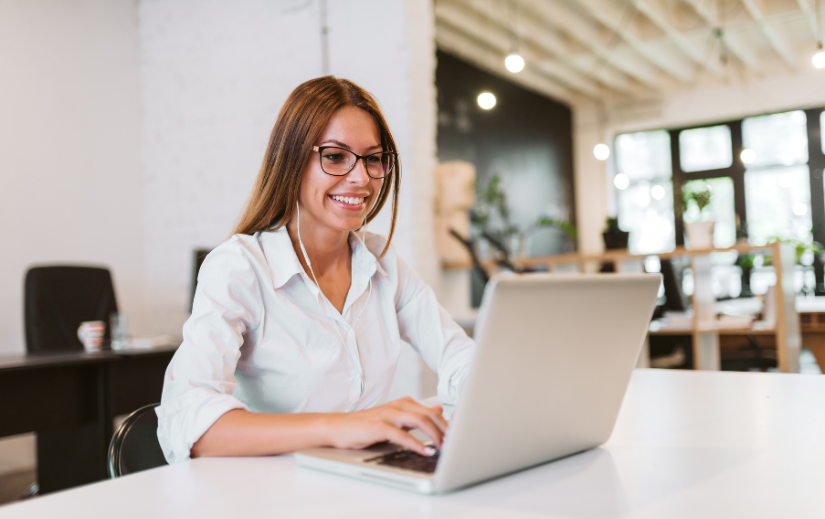 Smiling woman working on a laptop in a modern office, using the best tools for dropshipping to grow her business in 2025.